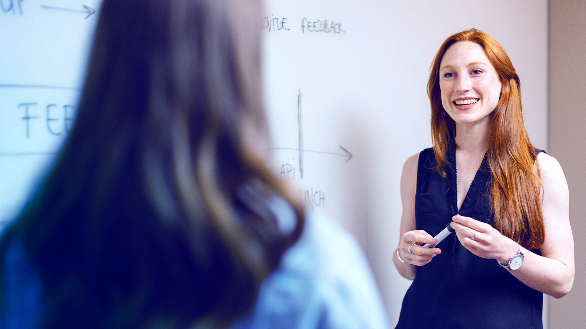 Two women standing in front of a whiteboard, featuring a chart.